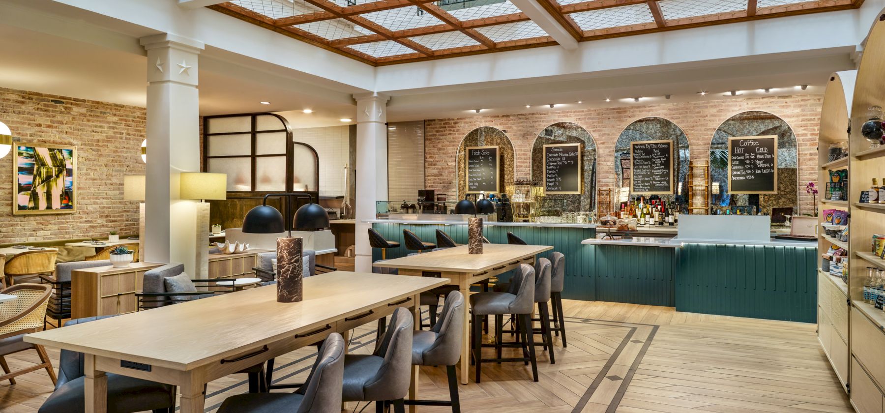 A cozy, modern cafe with wooden tables, cushioned chairs, a counter with pastries and drinks, large windows, and stylish decor in a bright atmosphere.