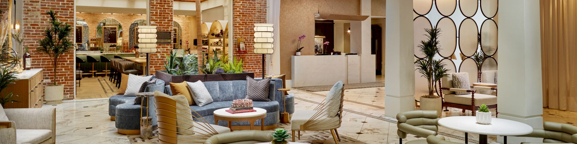 A modern, stylish lobby with a mix of armchairs, tables, sofas, and a reception desk in the background, featuring brick walls and contemporary decor.