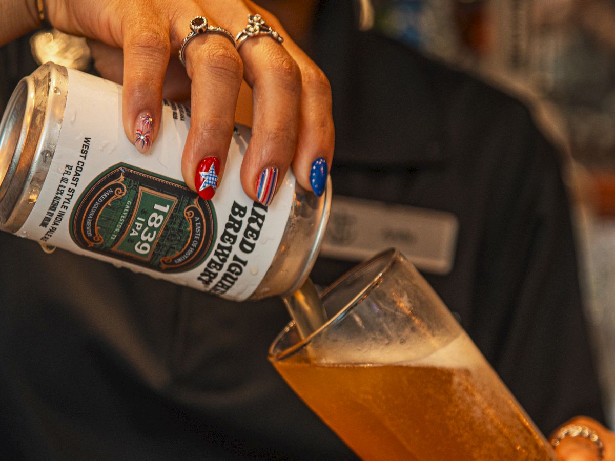 A person with jeweled rings and colorful nail art holds a can of beer, brushing a finger across the label.