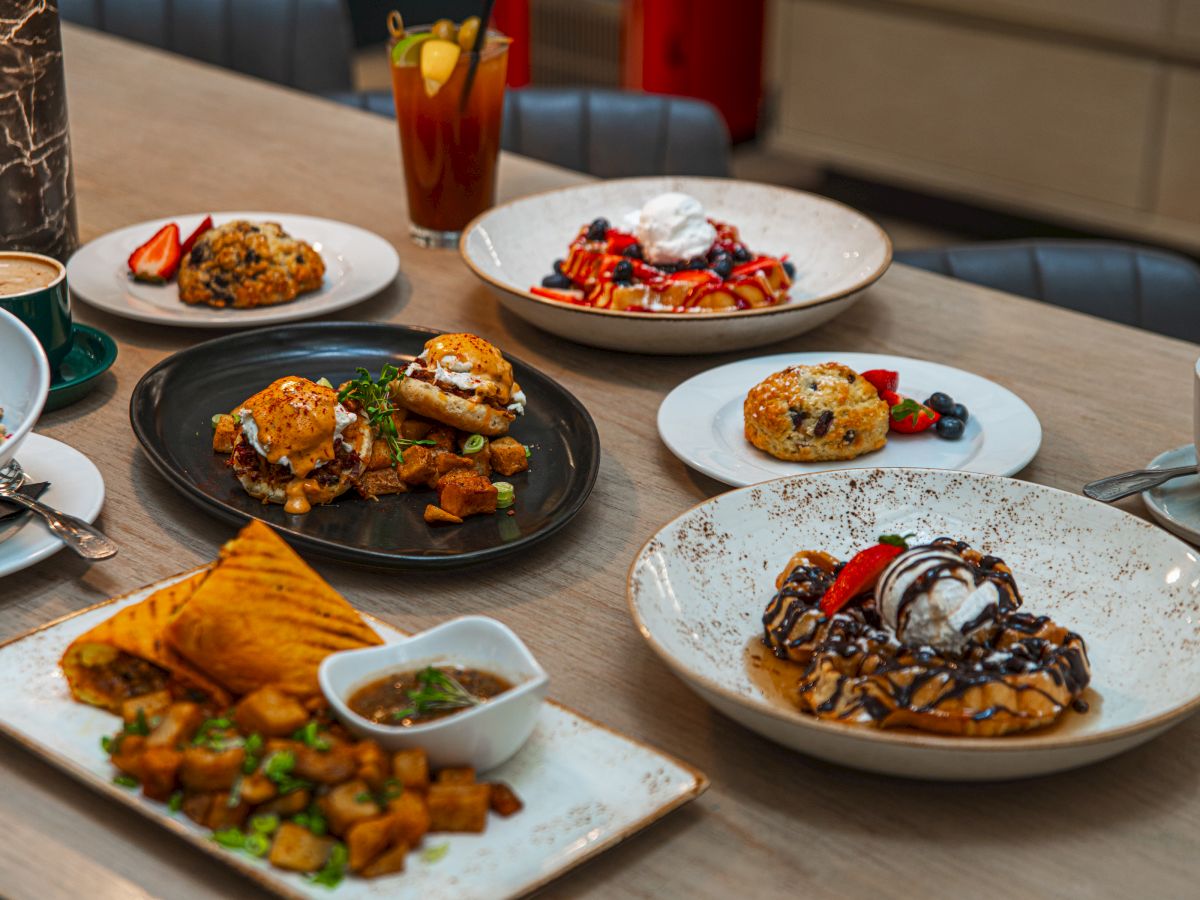 A dining table with multiple plated entrees, sides, and salads, plus drinks, all ready to eat.