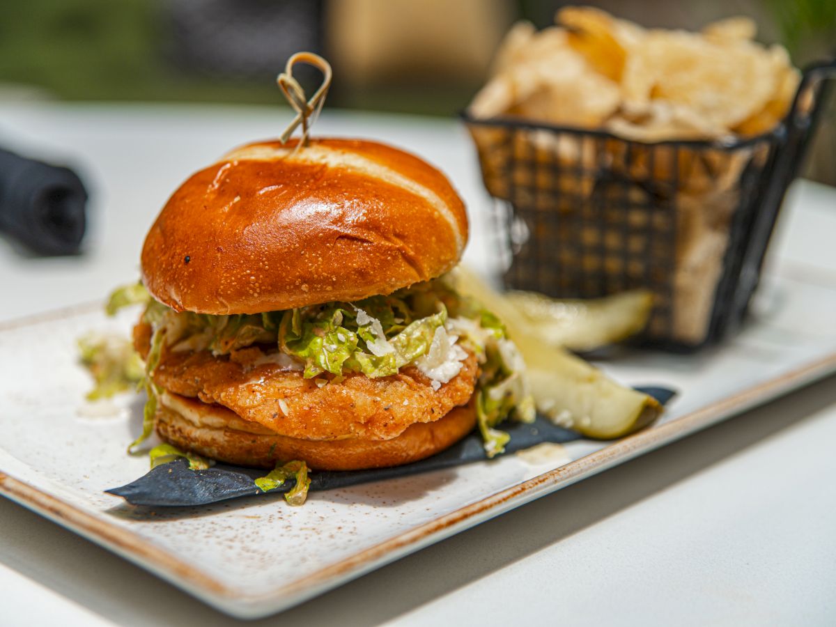 A stacked cheeseburger with lettuce and sauce on a plate, with fries in a basket in the background.
