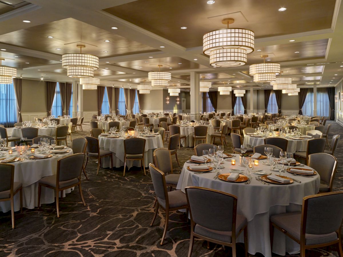 A large banquet hall with round tables set for an event, featuring elegant chandeliers, neatly arranged chairs, and dim lighting.