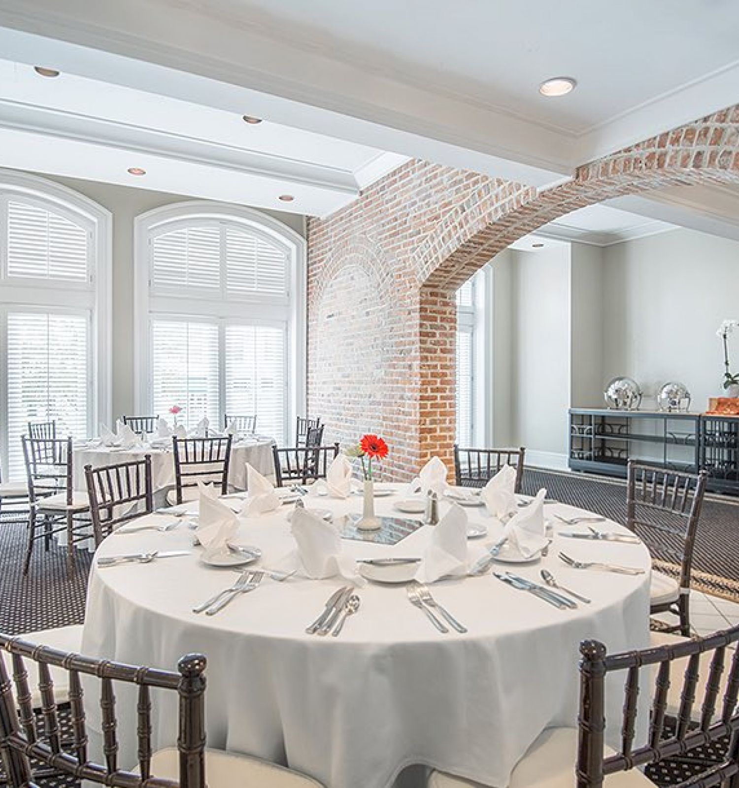 A dining room with round tables set with white tablecloths and neatly arranged cutlery. There's natural light coming through large windows.