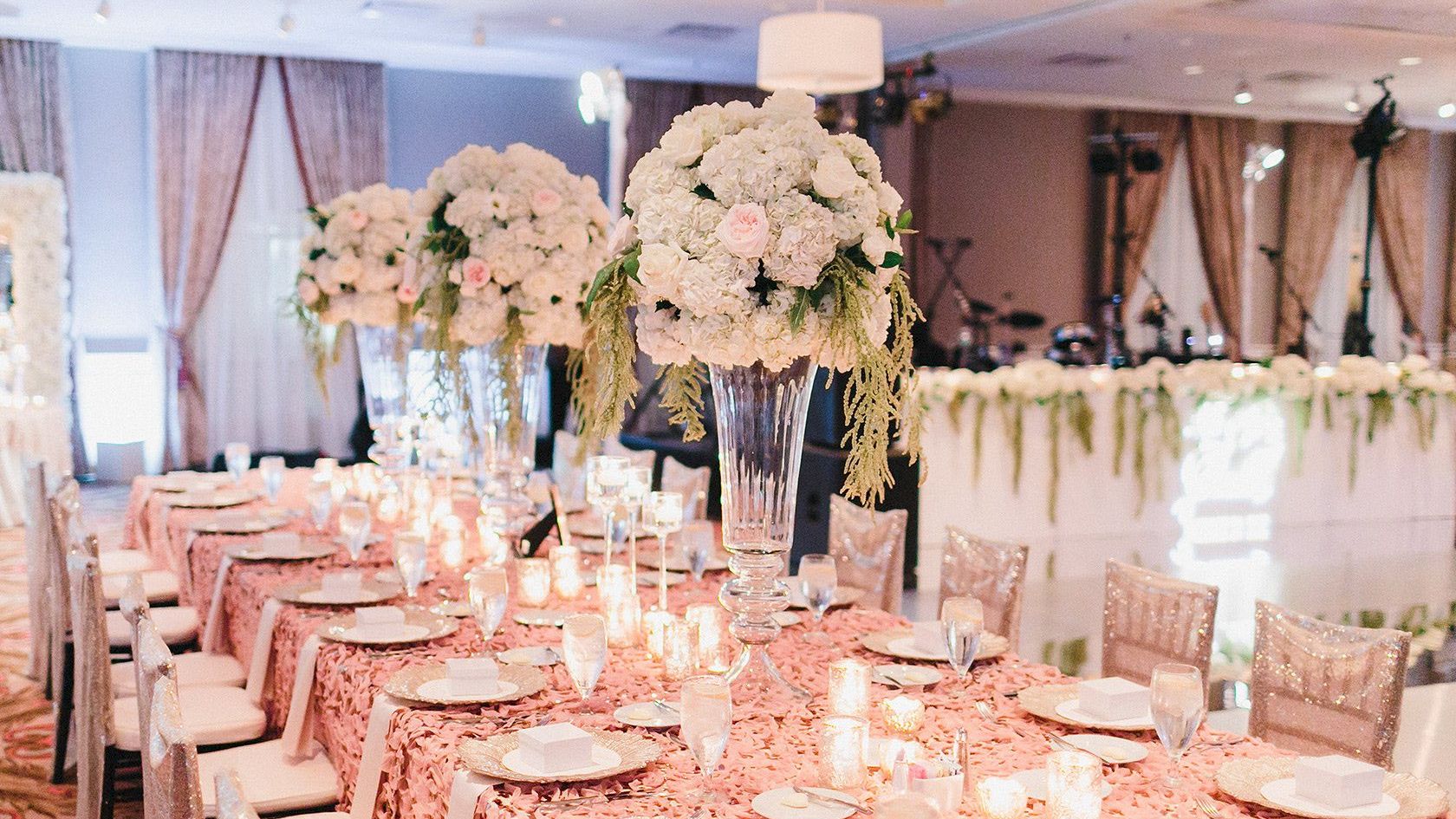 A beautifully decorated banquet hall with lavish floral centerpieces, elegant table settings, and ambient lighting.
