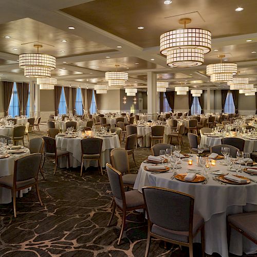 The image shows an elegantly set ballroom with round tables and chairs, chandelier lighting, and prepared for an event or dinner.