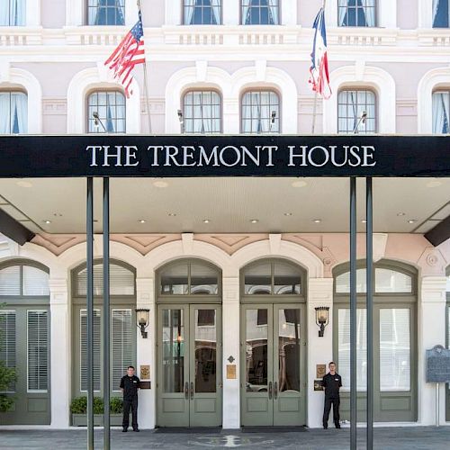 The image shows the entrance of The Tremont House hotel with two flags, elegant architecture, and two people standing at the doors.