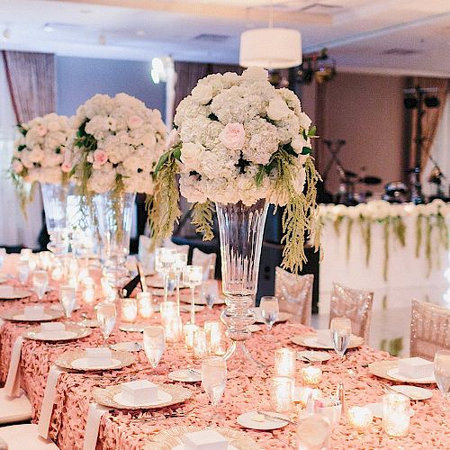 A beautifully decorated event table with floral centerpieces, candles, and elegant table settings in a luxurious indoor venue.