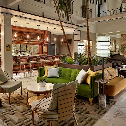 A stylish lobby with modern furniture, a green couch, chairs, tables, indoor plants, a bar area, and elegant lighting.