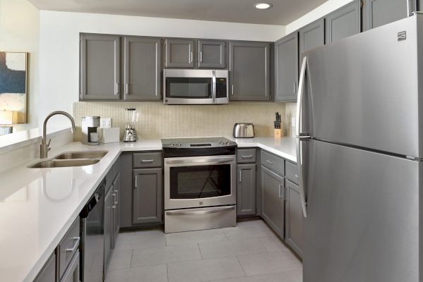 The image shows a modern kitchen with gray cabinets, stainless steel appliances, a refrigerator, a microwave, and a dual sink area, ending the sentence.