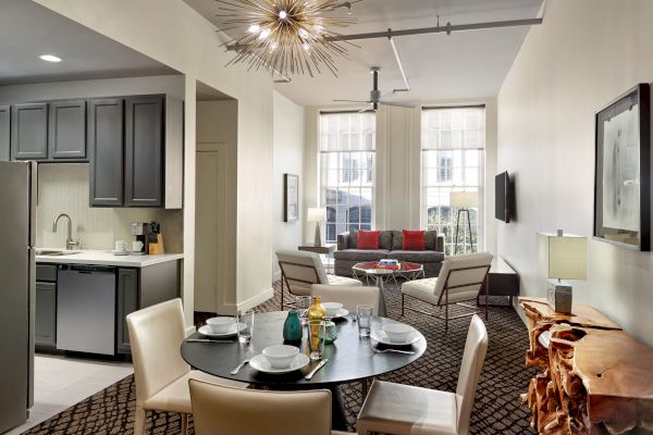 A modern apartment interior features a kitchen, a dining area with a round table set for four, and a living area with two chairs and a sofa.