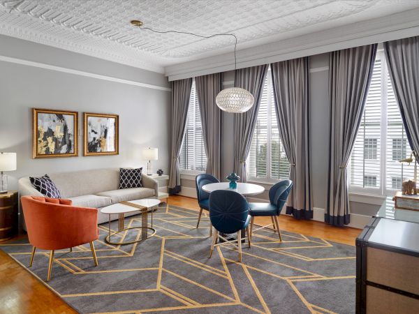 A stylish living room with a gray rug, elegant furniture, modern decor, large windows with curtains, and a unique ceiling light fixture.