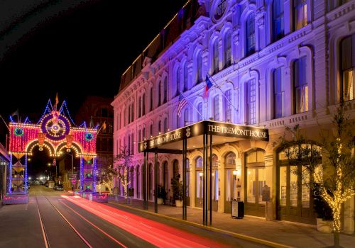 A beautifully lit street at night features an ornate building glowing with purple lights and a brightly illuminated archway in the background, creating a festive atmosphere.