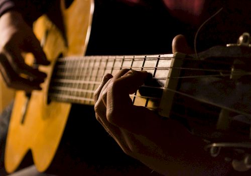 A person is playing an acoustic guitar with a focus on their hands strumming and pressing the strings.