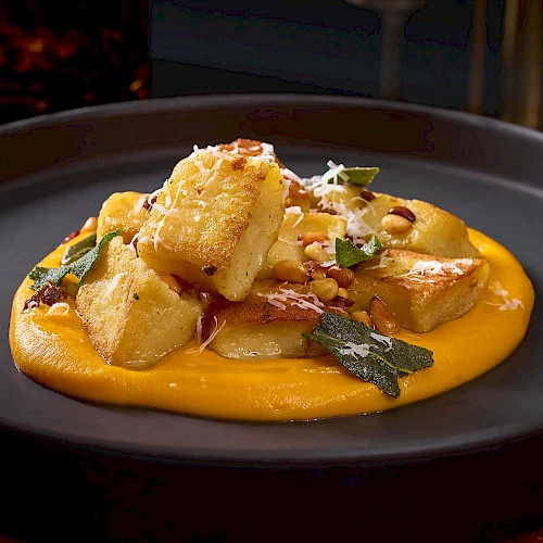 Golden gnocchi on a bed of creamy orange sauce, topped with grated cheese and herbs, served on a dark plate.