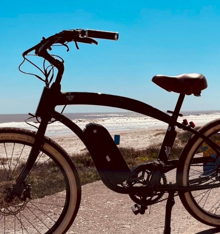 A black electric bike stands on a desert road under a clear blue sky.