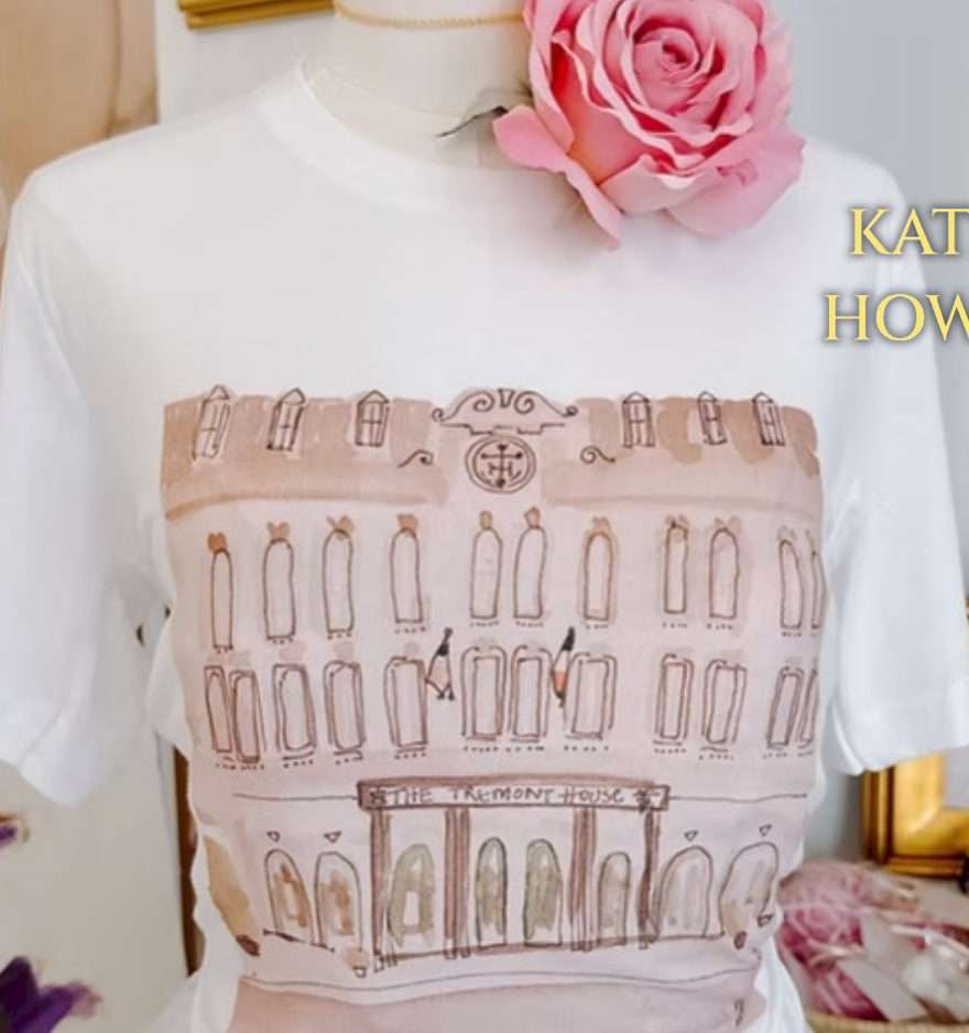 A white T-shirt displaying a row of door-like figures, styled with a pink rose and &ldquo;KATRINA HOWARTH&rdquo; text on a dressed display.