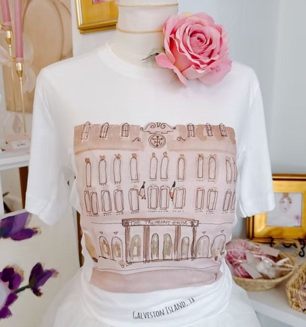 A white shirt on a mannequin with a brown building/candle print, topped by a large pink rose accessory.