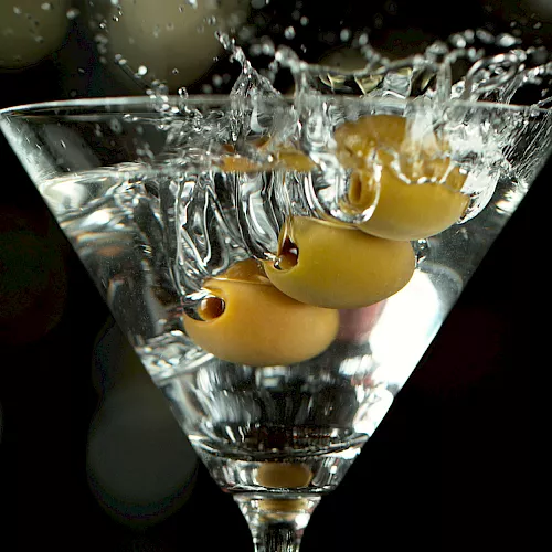 A martini glass filled with amber liquid is caught mid-splash, with bubbles and droplets bursting upward.